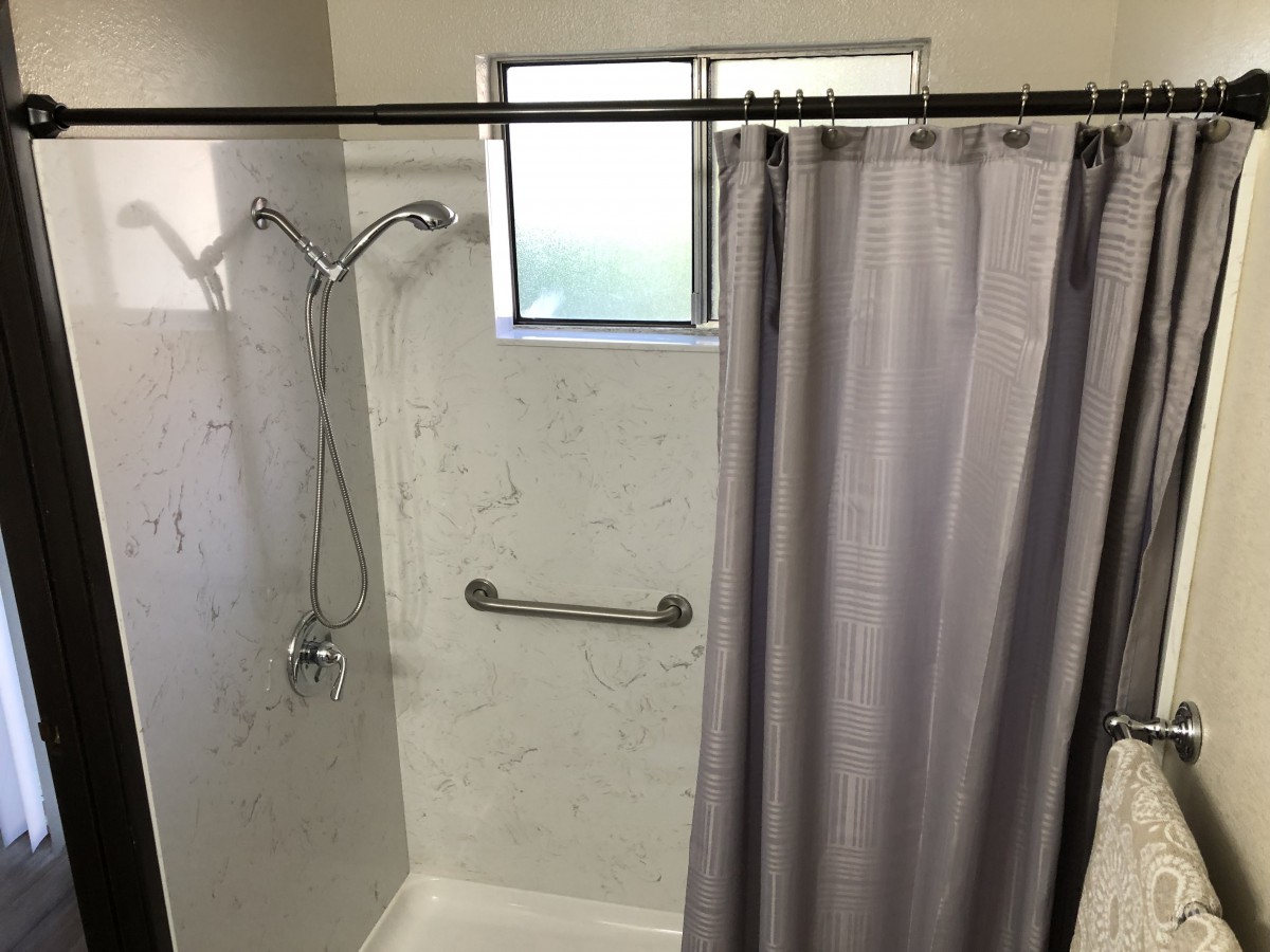A shower area with a curtain, window, and grab bar.