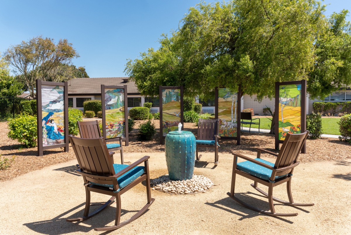 A cozy outdoor patio area features several chairs arranged around a central table, set amidst lush garden landscaping.