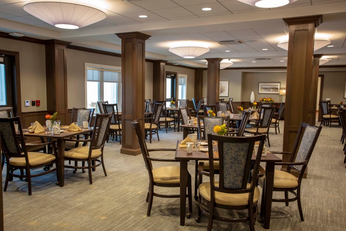 An elegant dining area with neatly arranged tables and chairs, featuring warm lighting and wooden accents.