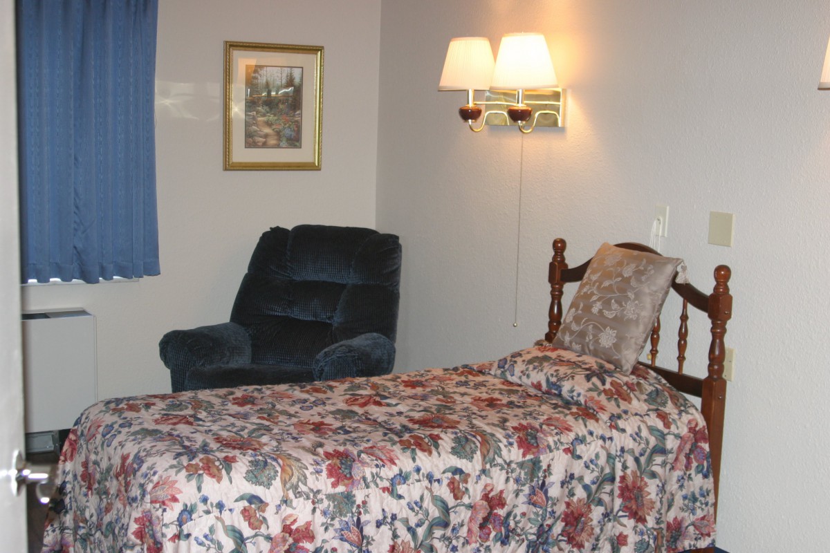 A cozy bedroom with floral bedding, an armchair, and wall lamp.