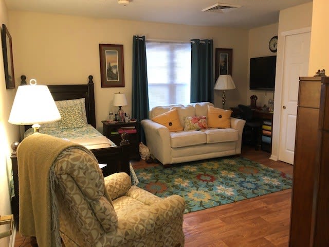 A cozy combined living and bedroom area with a sofa, bed, armchair, and TV.