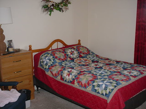 A cozy bedroom featuring a wooden bed with a colorful quilt and a chest of drawers.