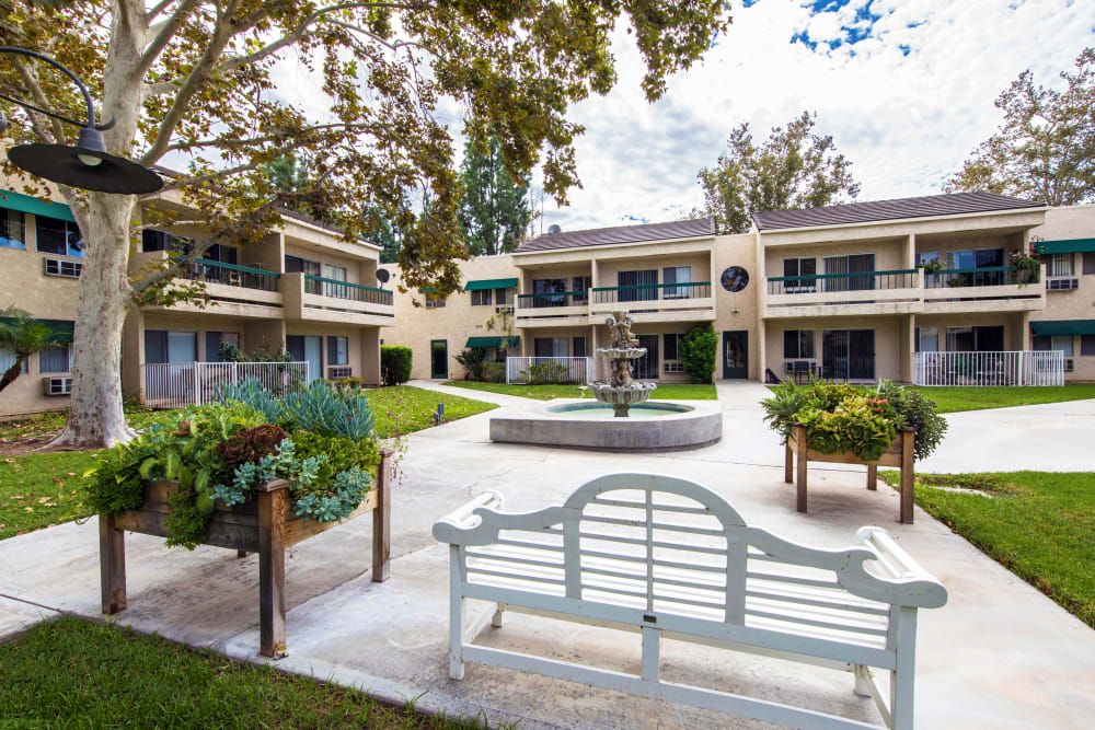 A peaceful courtyard featuring a central fountain and a bench surrounded by landscaped greenery and residential buildings.