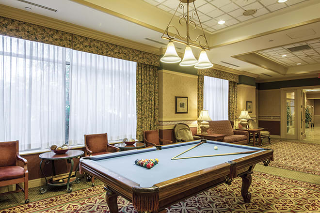 A cozy billiard room featuring a pool table with lighting fixtures overhead and comfortable seating around.