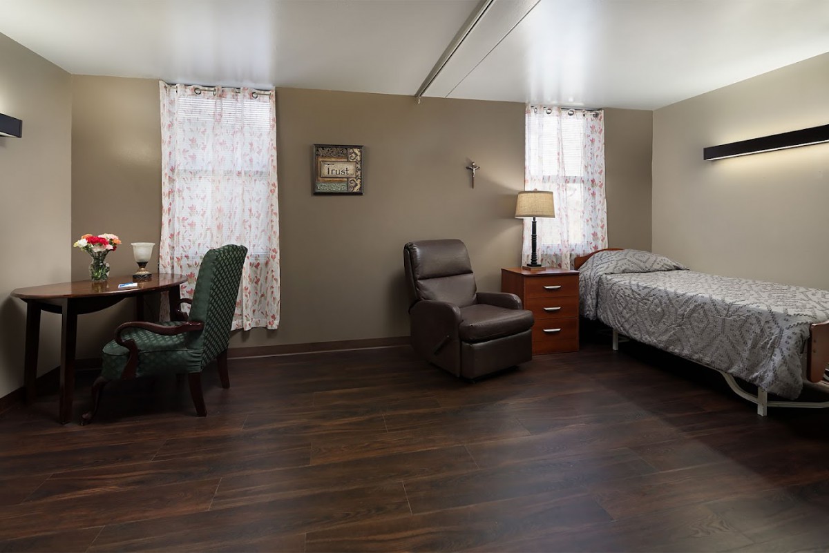 A neatly arranged bedroom with a bed, recliner, desk, and lamp.