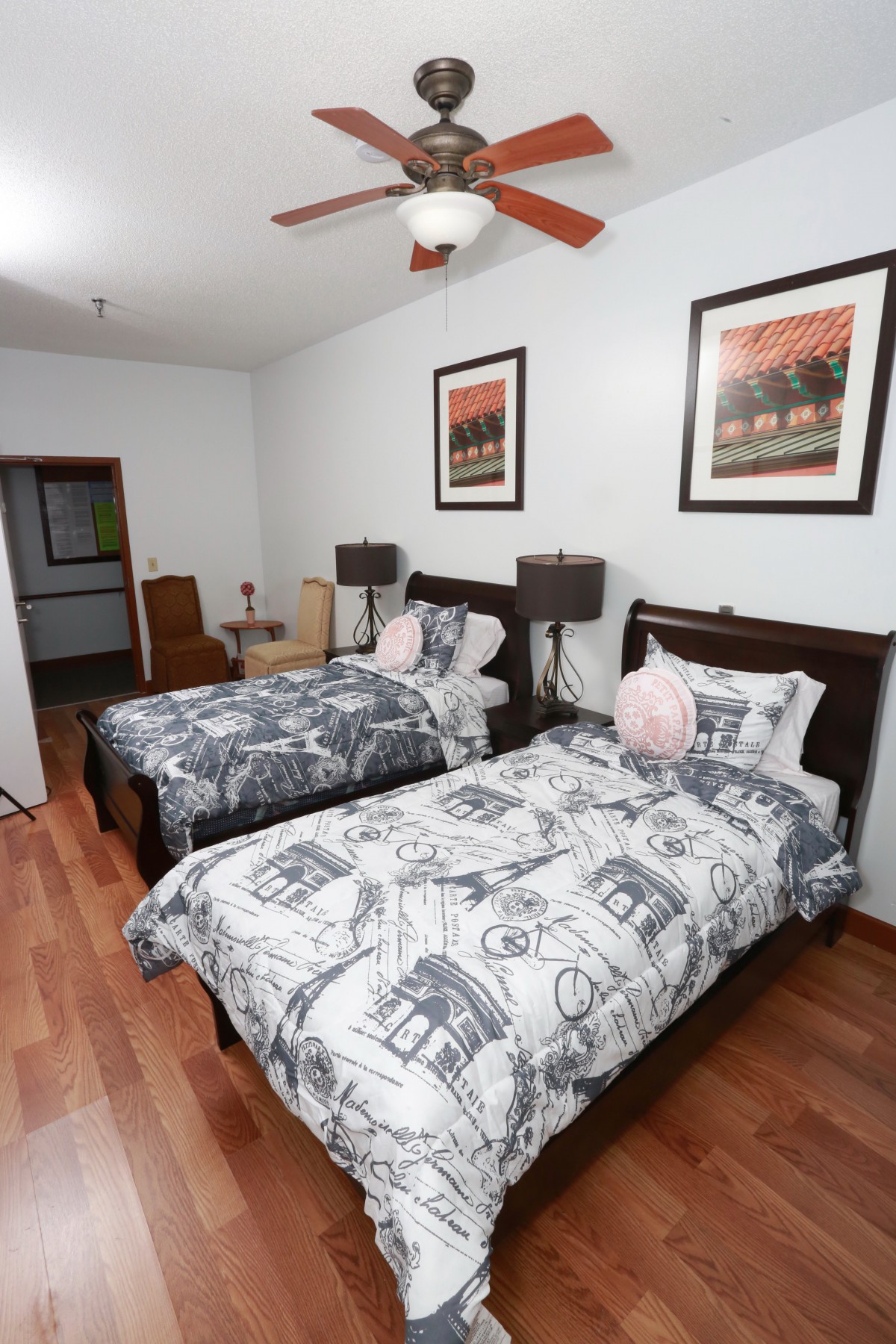 A cozy bedroom featuring two twin beds with patterned bedding, adorned with bedside lamps and framed artwork on the walls.