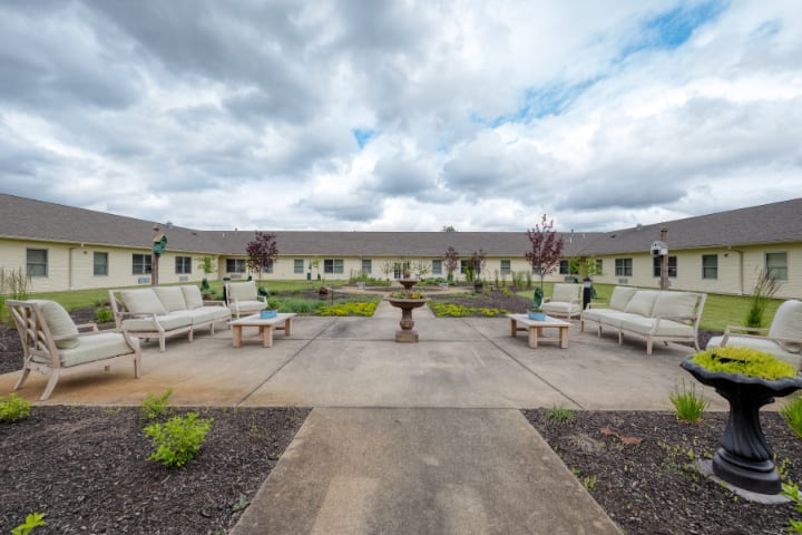 A serene courtyard featuring benches, a central fountain, and manicured landscaping under a cloudy sky.