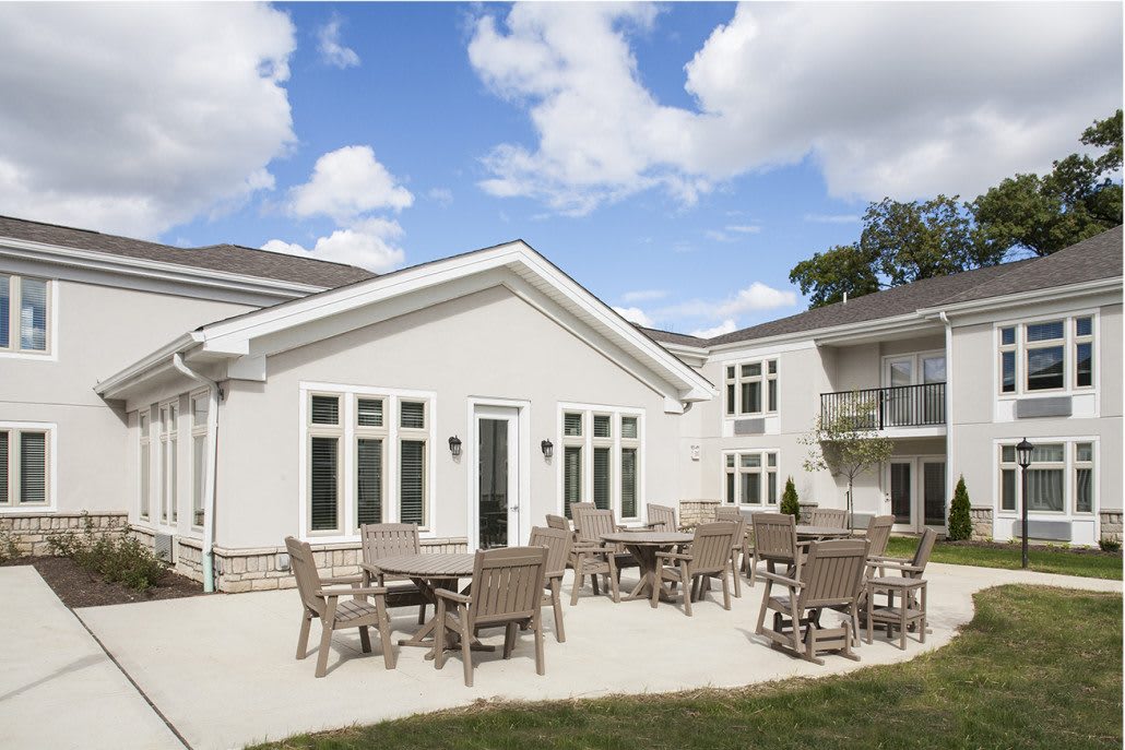 A spacious outdoor patio area with tables and chairs against a modern building backdrop under a partly cloudy sky.