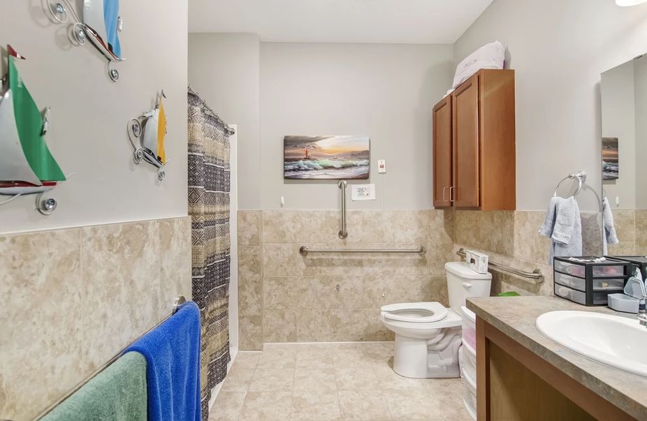 A modern bathroom with a shower, toilet, and cabinets, decorated with towels and artwork.