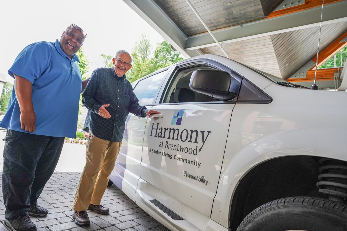 Two men standing beside a community vehicle with 'Harmony at Homewood' logo.