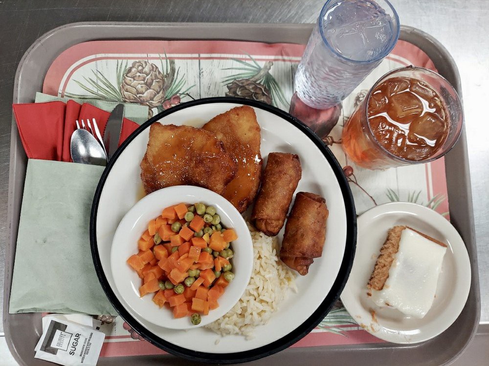 A meal served on a tray with fish, rice, spring rolls, mixed vegetables, a drink, and dessert.