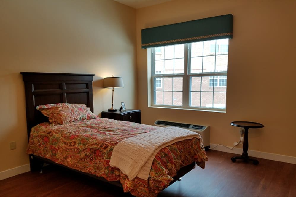 A cozy bedroom with a single bed, lamp, and window.