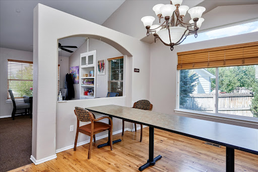 A cozy dining area featuring a modern chandelier, a long table with chairs, and ample natural light from the window.