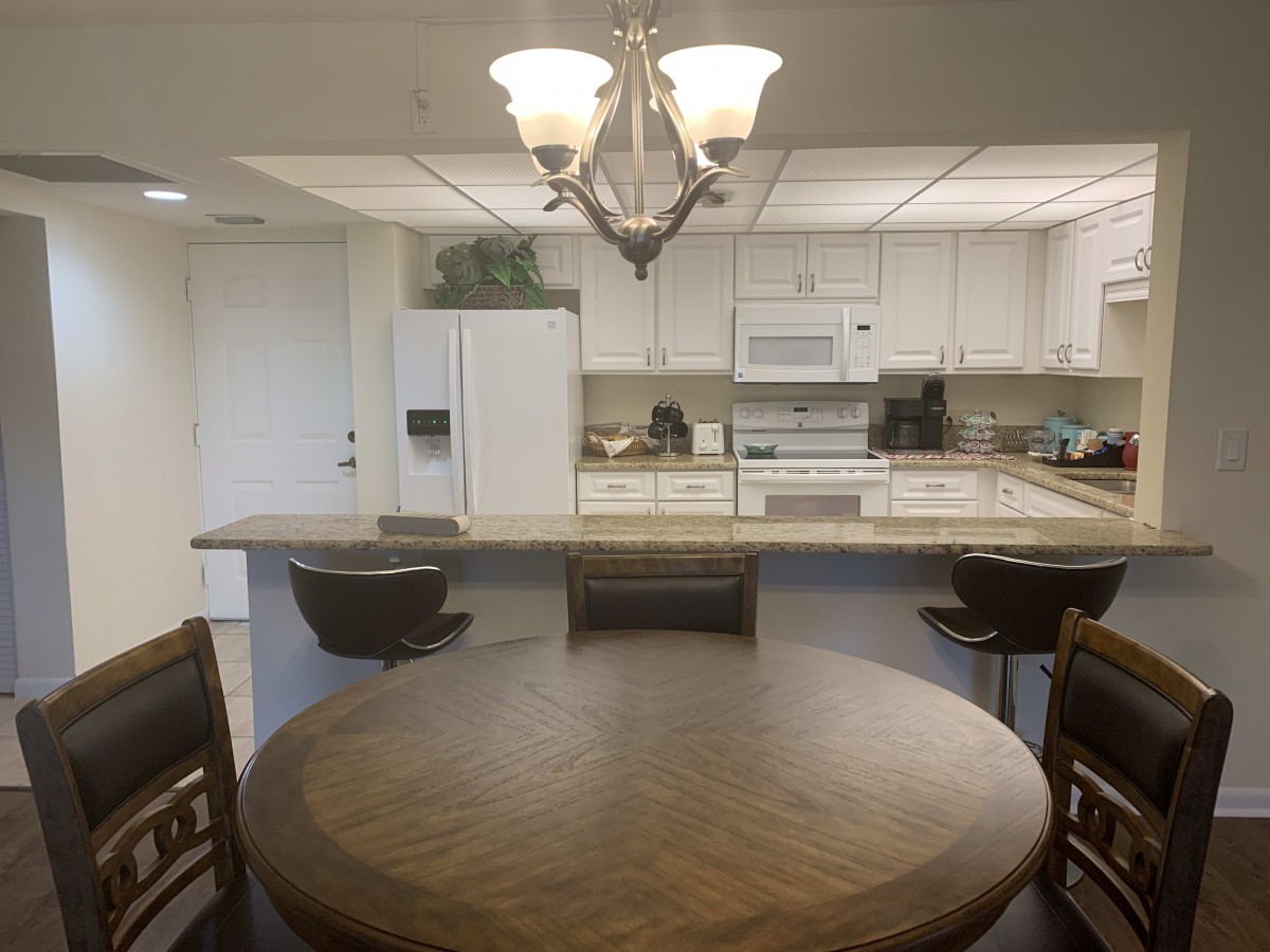 A cozy kitchen and dining area featuring a round wooden table, a chandelier, and white cabinetry with appliances.