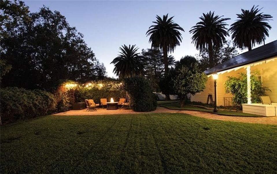 A tranquil garden with palm trees and cozy outdoor seating lit by warm evening lights.