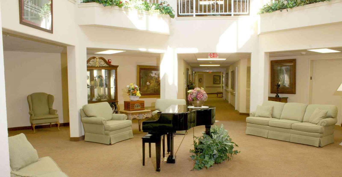 A spacious lobby featuring a grand piano and comfortable seating, surrounded by natural light and decorative plants.