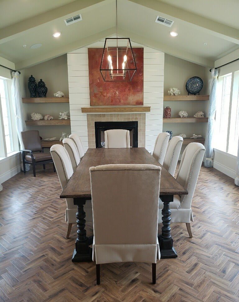 A well-decorated dining room with a large wooden table, upholstered chairs, and a central fireplace.