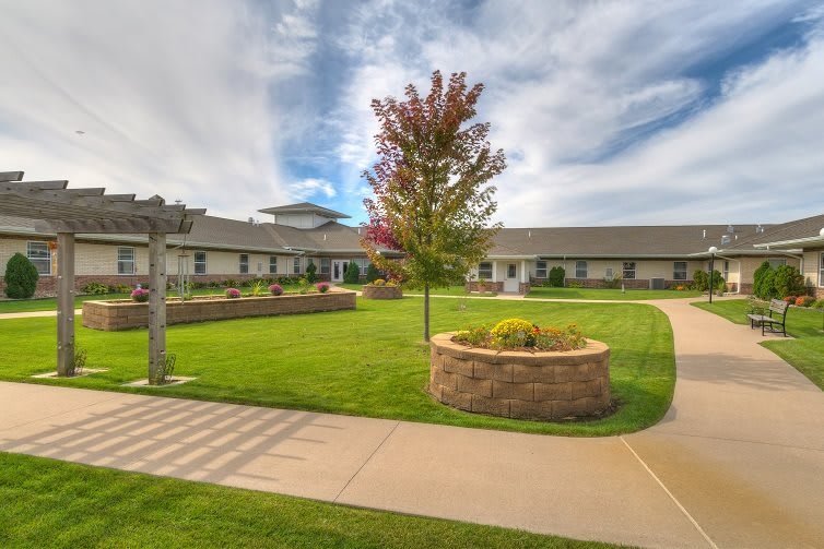 A scenic view of a building with a well-maintained lawn, trees, and clear pathways under a cloudy sky.