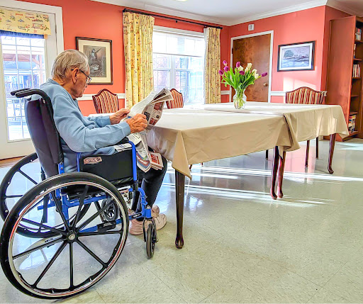 An elderly person sitting in a wheelchair, engrossed in reading inside a care facility.