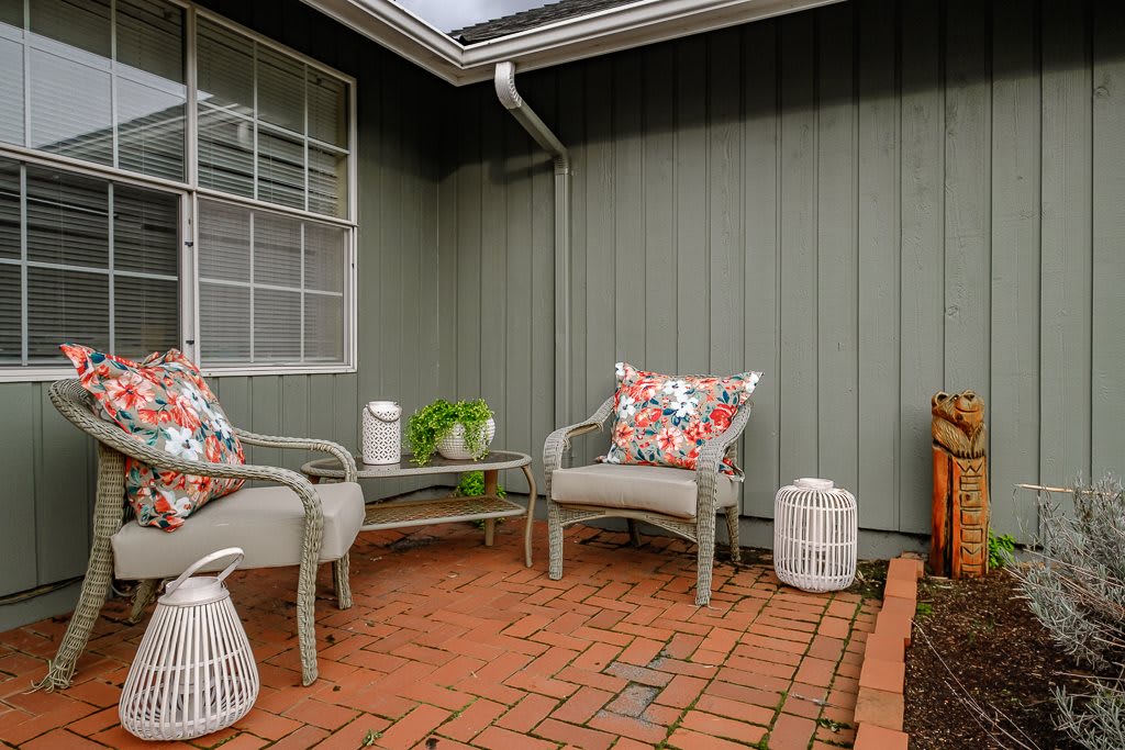 Cozy patio area with brick flooring and outdoor seating, featuring colorful pillows and decorative plants.