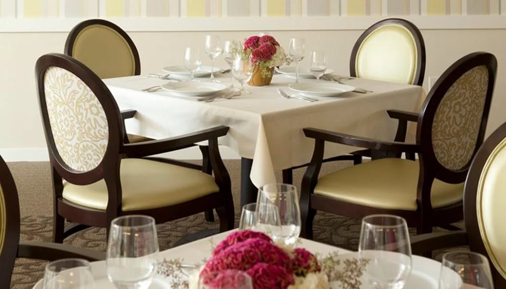 An elegantly set dining table in a restaurant with flowers and glassware.