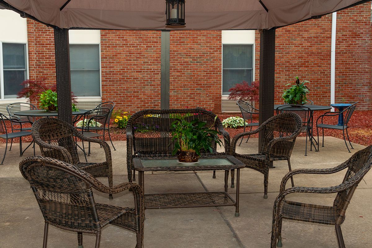 A cozy patio area featuring wicker furniture and potted plants against a brick wall backdrop.