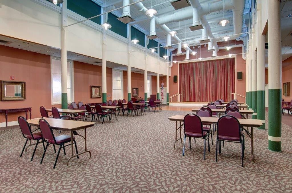 An empty conference room with a stage, featuring tables and chairs arranged for an event.