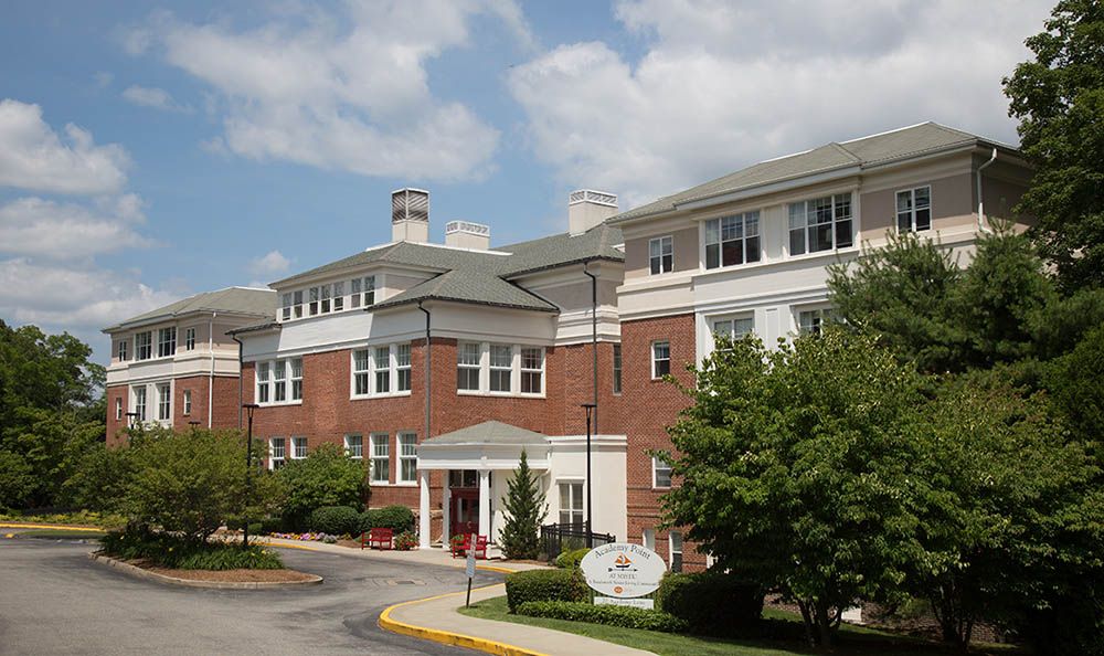 A residential building with a red brick facade surrounded by trees under a partly cloudy sky.