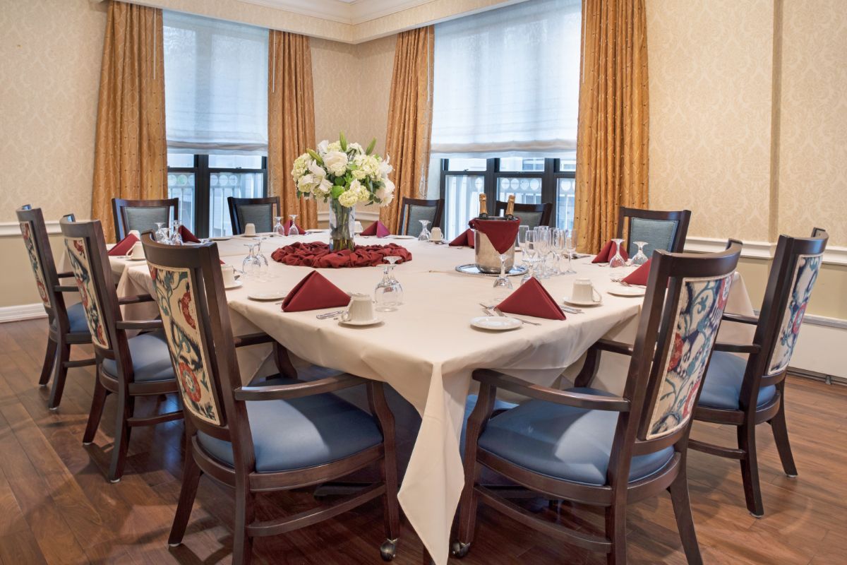 An elegantly set dining room with a round table, adorned with a white tablecloth, red napkins, and a floral centerpiece.