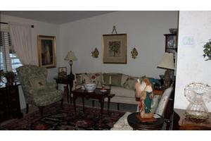 A cozy living room with traditional decor, featuring a sofa, armchair, and various artworks on the walls.