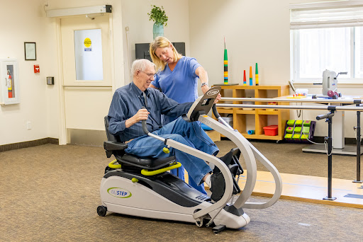 A healthcare professional assists a senior patient with exercise on specialized equipment during a rehabilitation session.