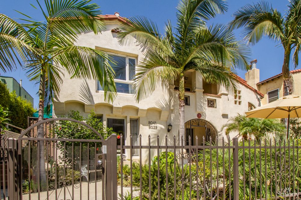 A tropical-style house with palm trees and a gated entrance.
