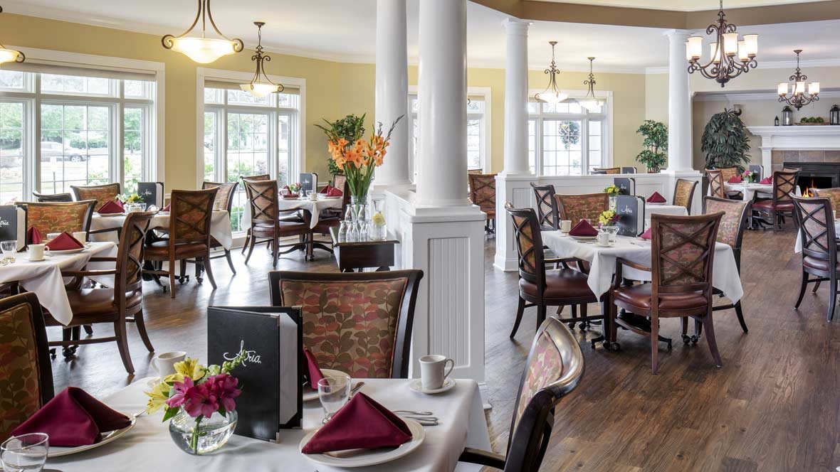 An elegant dining room with neatly arranged tables and chairs, featuring floral decor and ambient lighting.