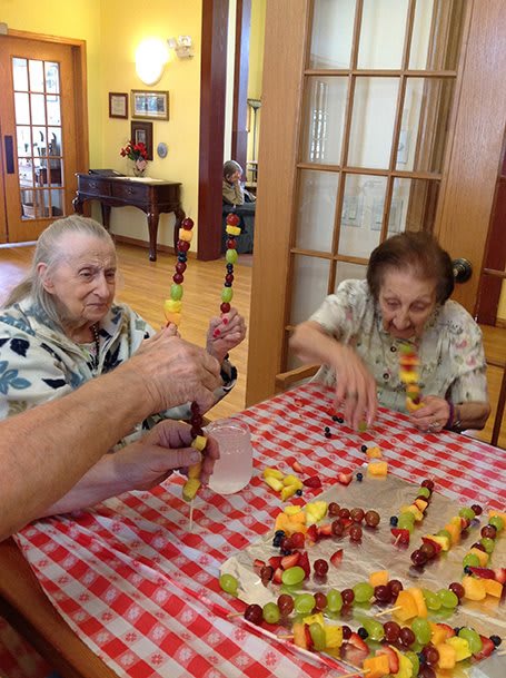 Elderly individuals enjoying making fruit kabobs together at a table.