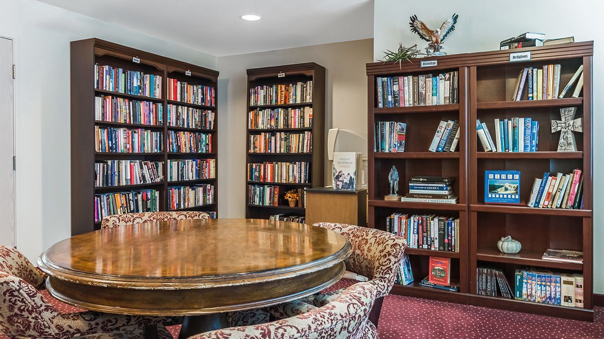 A cozy library corner with bookshelves filled with books and a round wooden table surrounded by patterned chairs.