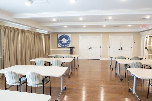A well-lit conference room with neatly arranged tables and chairs, set up for a meeting or presentation.