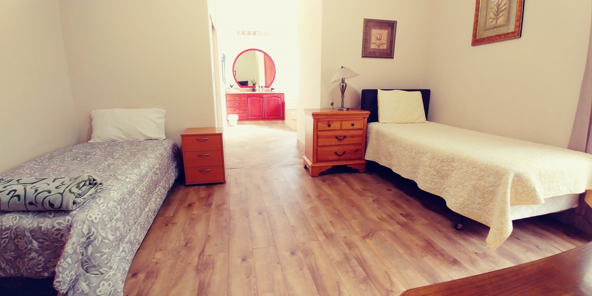 A cozy bedroom featuring two single beds and wooden furniture, with a dresser and mirror in the background.
