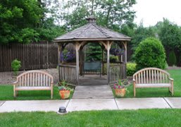 A quaint wooden gazebo surrounded by greenery with benches and potted plants.