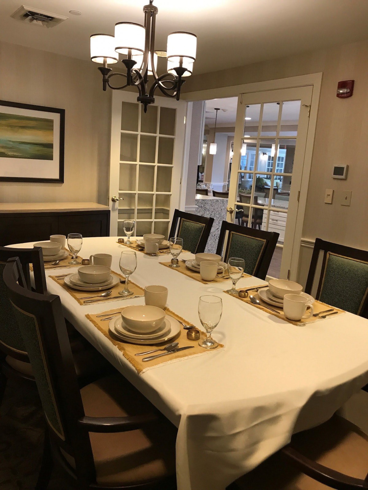 A dining room with a table set for a meal, featuring plates, glasses, and a chandelier.
