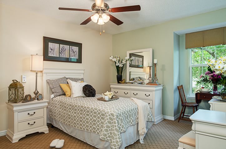 A cozy bedroom with a single bed, decorated with a neutral color palette and featuring a ceiling fan.