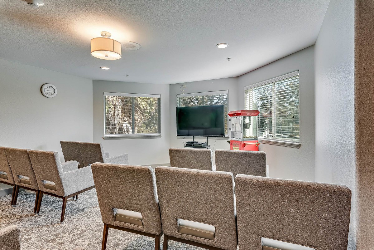 A cozy home theater setup with rows of chairs, a large TV, and a popcorn machine by the window.