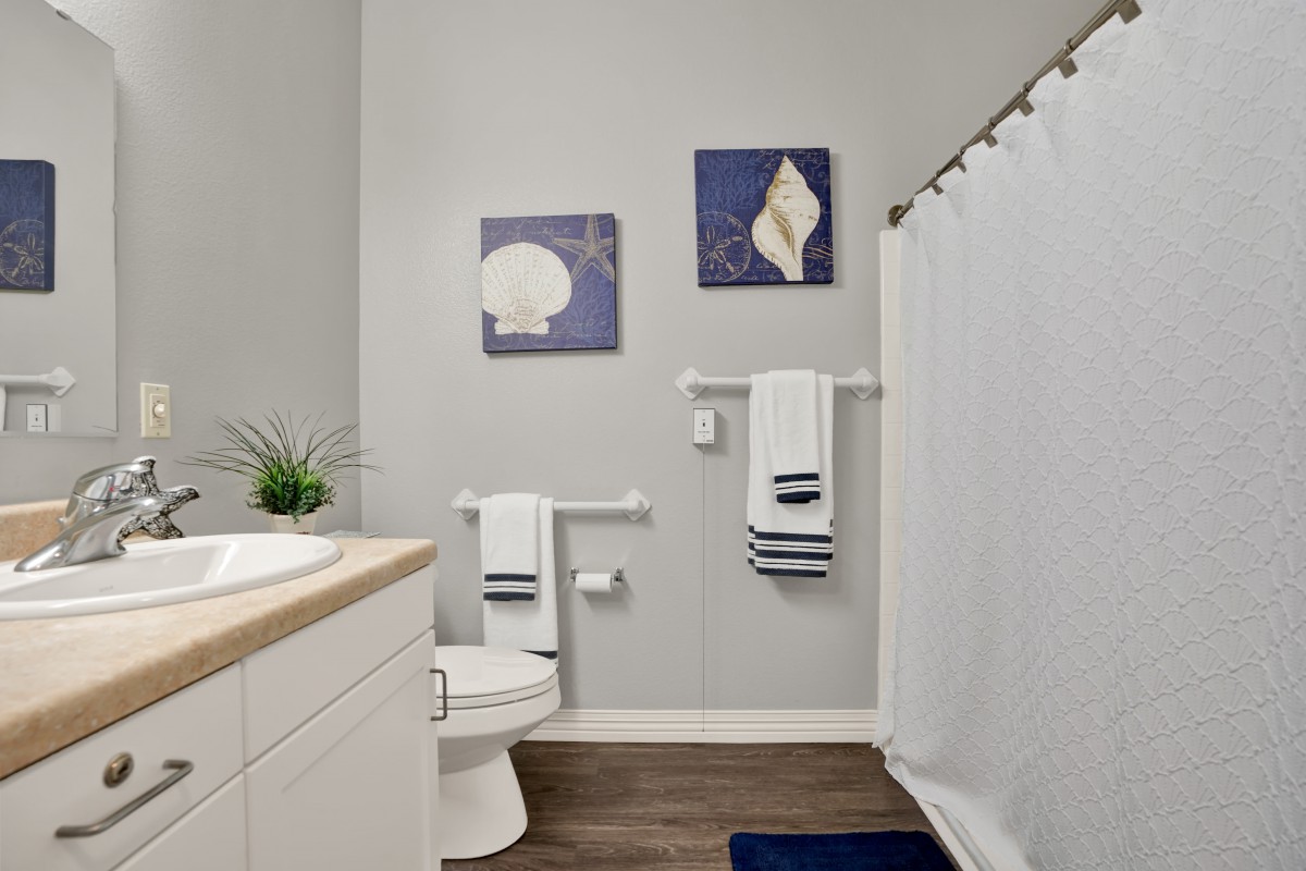 A modern, minimalist bathroom with light gray walls, decorative wall art, and organized towels.