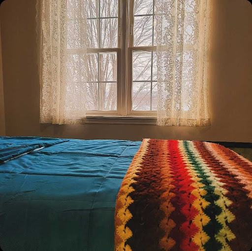 A cozy bedroom with a view, featuring a colorful blanket draped over the bed and warm natural light filtering through the window.