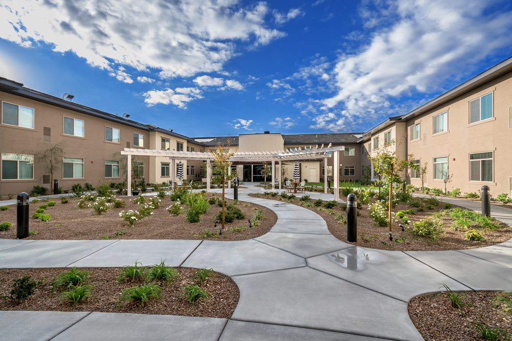 A modern building with a landscaped garden and pathway under a bright blue sky with clouds.