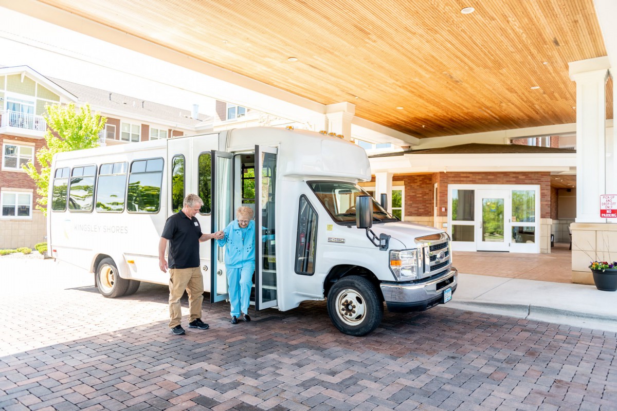 A shuttle bus parked at the entrance of a building, with people exiting.