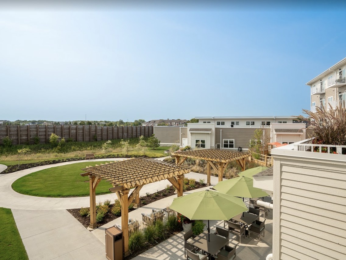 A sunny outdoor courtyard with pergolas, a green lawn, and seating areas.