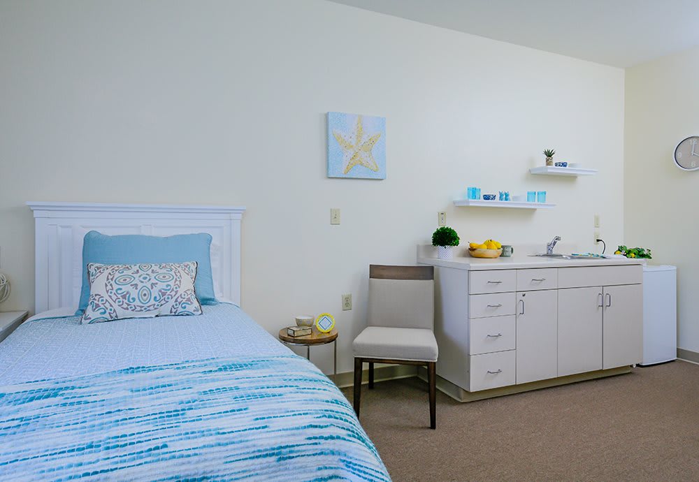 A cozy bedroom with a blue-themed bed, a chair, and storage cabinets alongside shelves with decorative items.