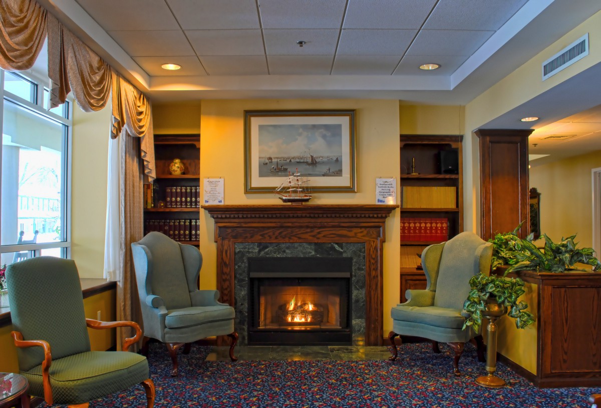 A cozy living room featuring a fireplace, surrounded by armchairs and bookshelves.