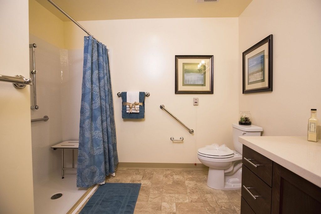 A well-organized bathroom featuring a shower with a blue curtain, towel rack, toilet, and framed wall art.