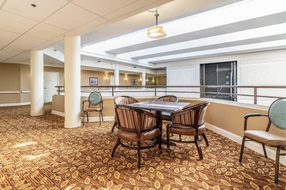 A cozy lounge area with a table and chairs, featuring warm lighting and patterned carpet.